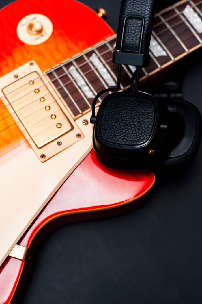Close-up of a red electric guitar paired with black wireless headphones on a dark background.