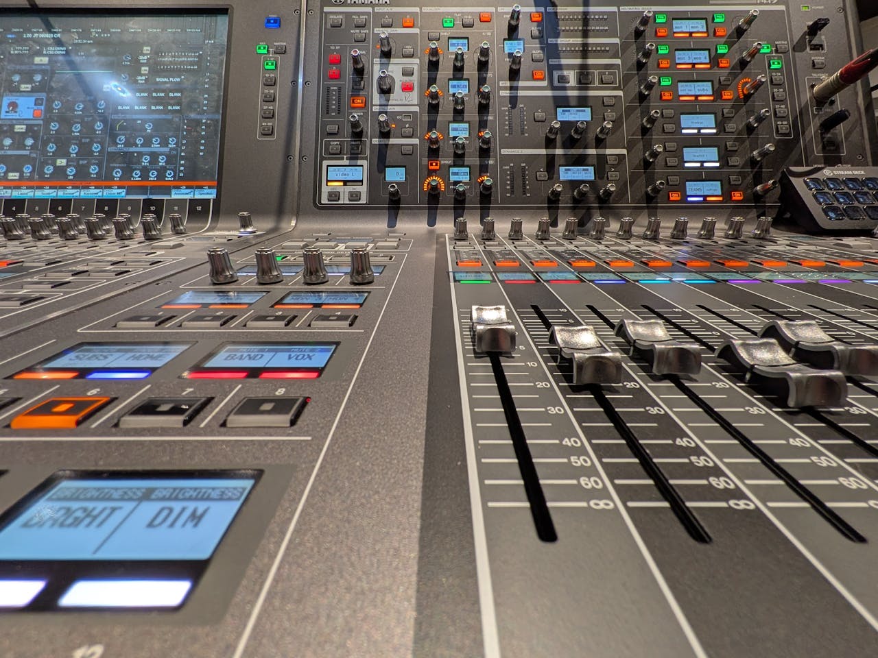 Close-up view of a professional audio mixing console with sliders and buttons in a studio setting.